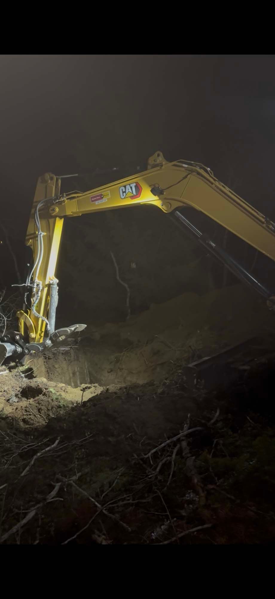 Yellow excavator digging at night in a dark, smoky construction site