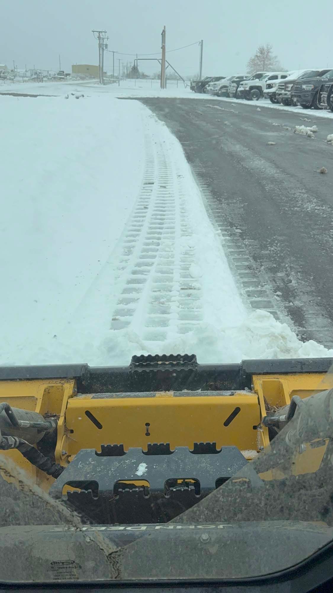 Snowplow clearing a snow-covered road beside parked cars in heavy snowfall