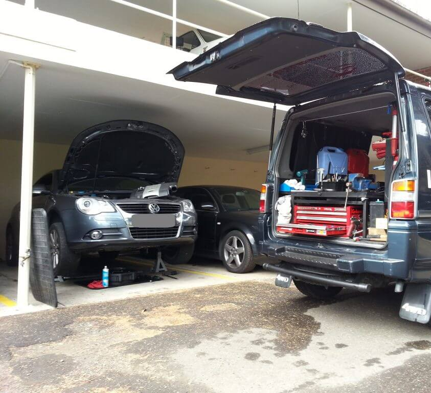 Two cars are parked in a garage with their hoods open