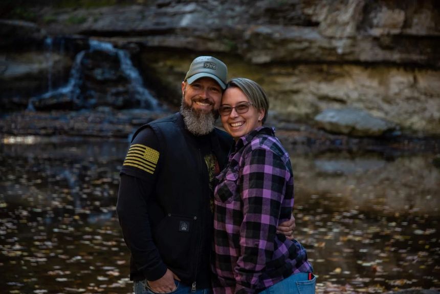 Smiling couple in outdoor gear posing by a rocky waterfall stream
