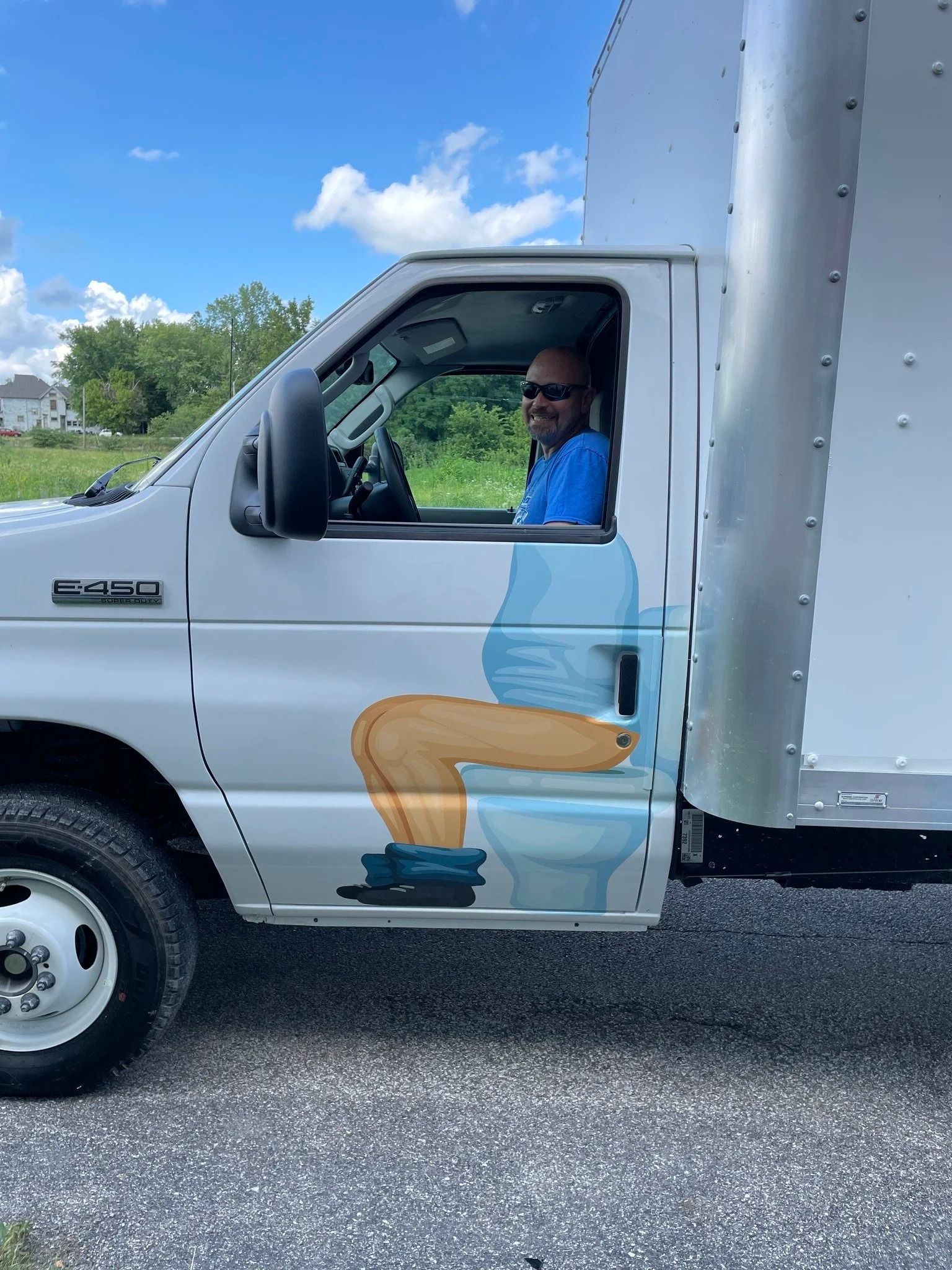 Man in blue shirt sits in a white box truck, smiling at the driver-side window.