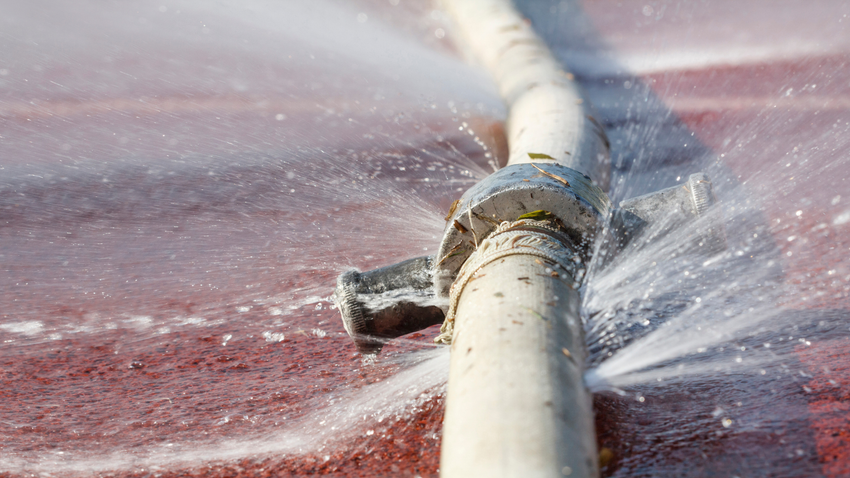 White hose spraying water over a red surface, creating a splash.