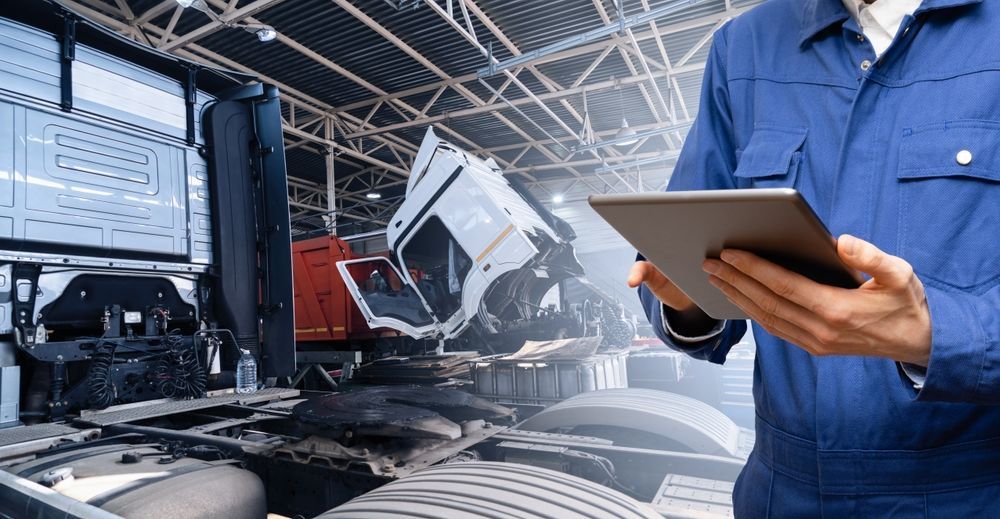 A man is holding a tablet in front of a truck in a garage.