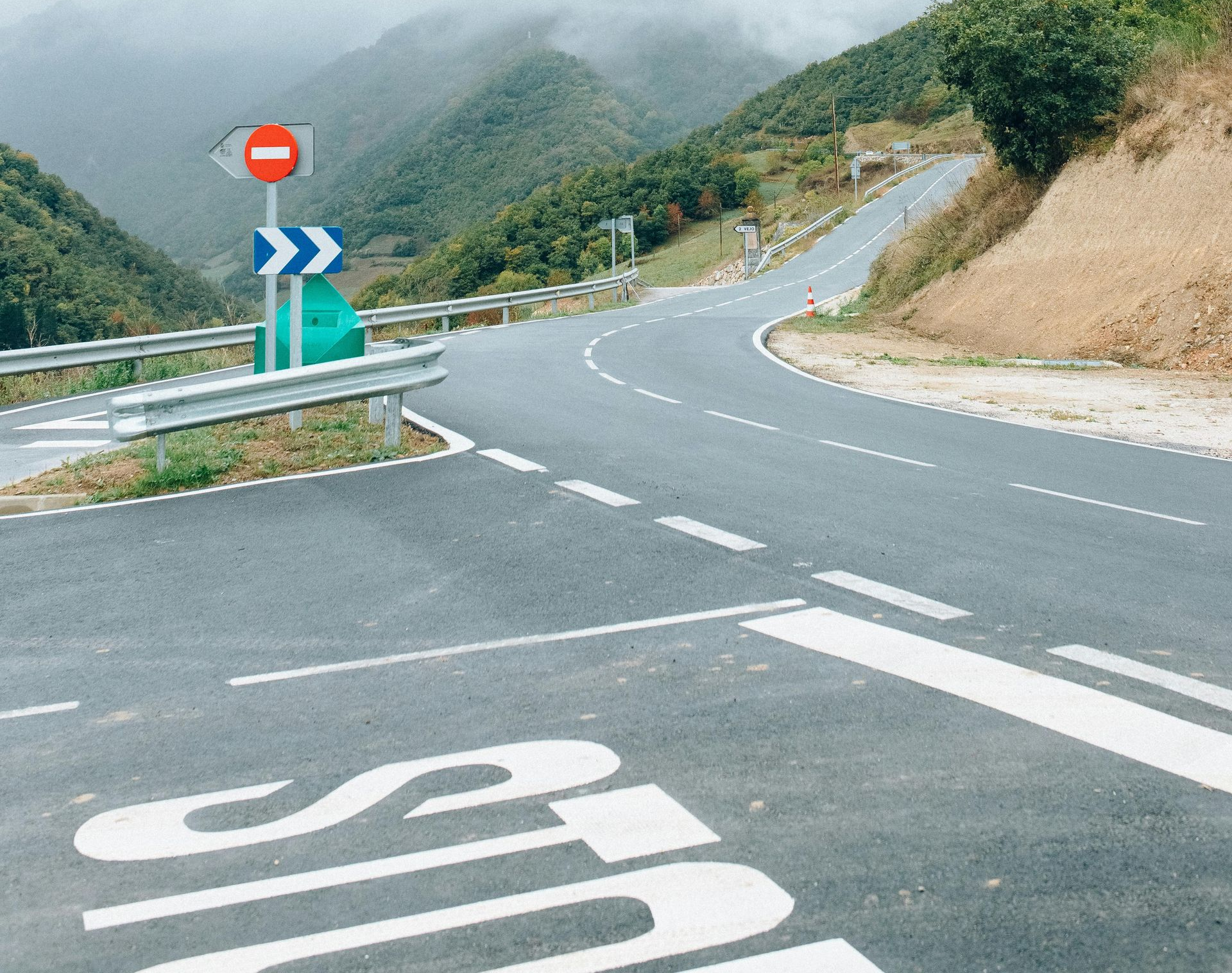 Winding mountain road with a no-entry sign on a cloudy day.