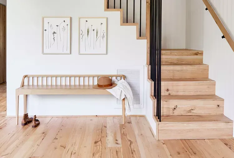 A wooden bench is sitting next to a wooden staircase in a hallway. A wooden bench is sitting next to a wooden staircase in a hallway.