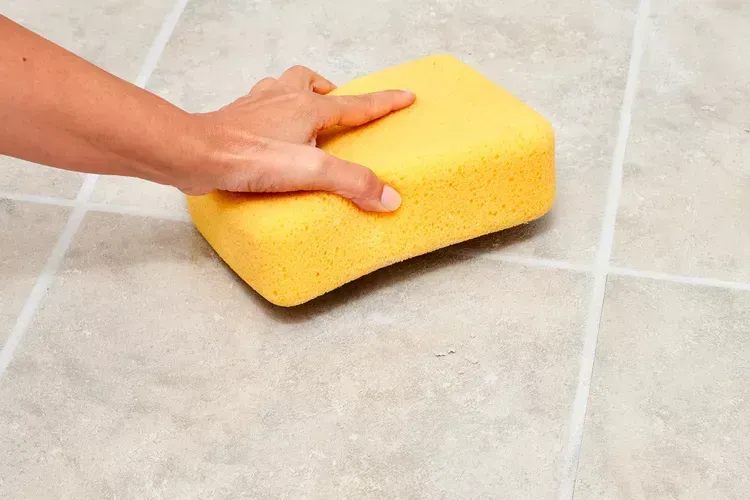 Someone cleaning a tile floor with a yellow sponge. Someone cleaning a tile floor with a yellow sponge.