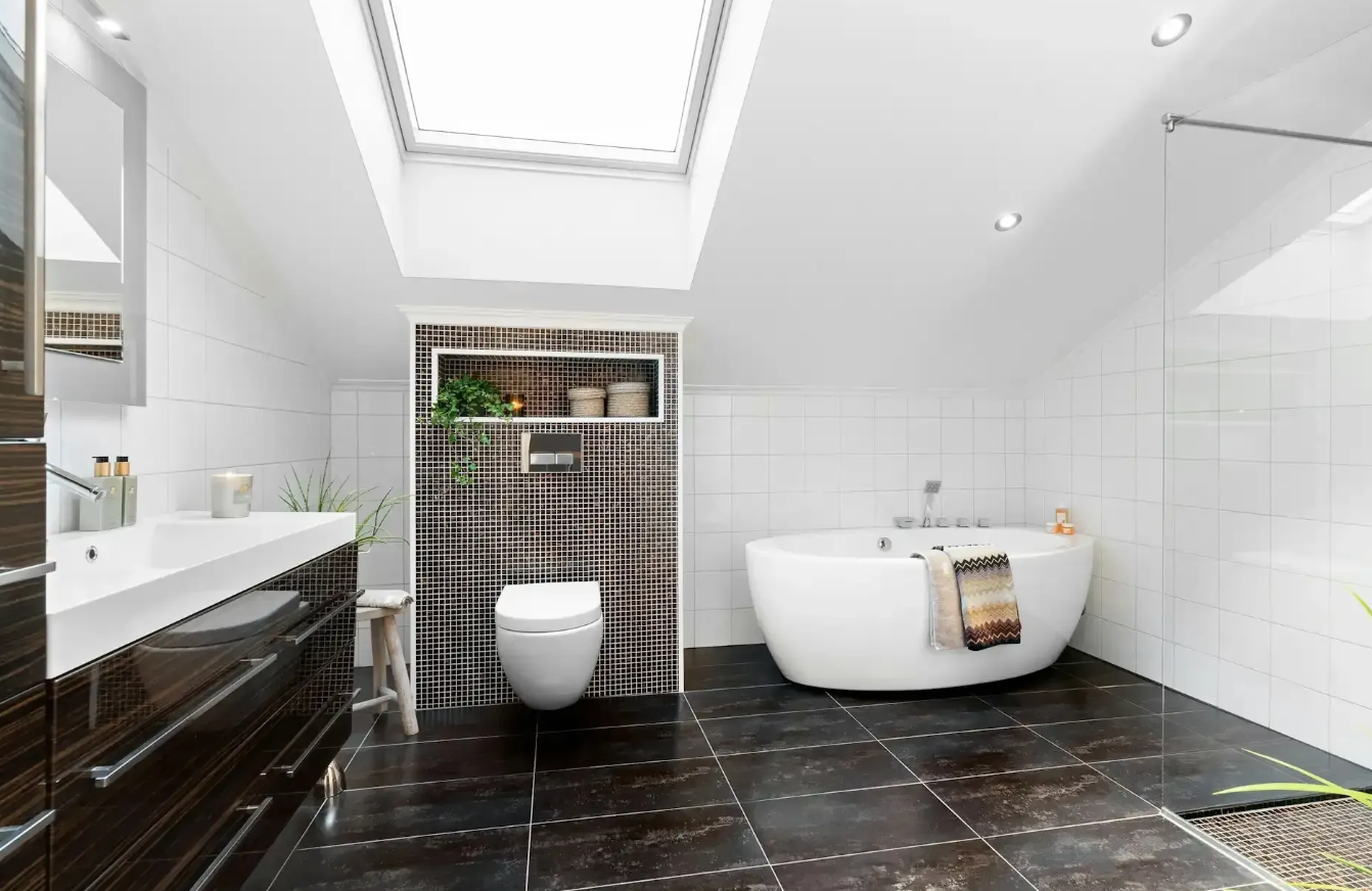 Modern attic bathroom with a soaking tub, dark tiles, wall-mounted toilet, and skylight.