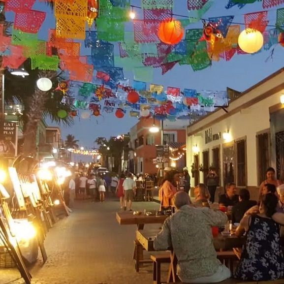 a group of people are sitting at tables under a string of colorful flags