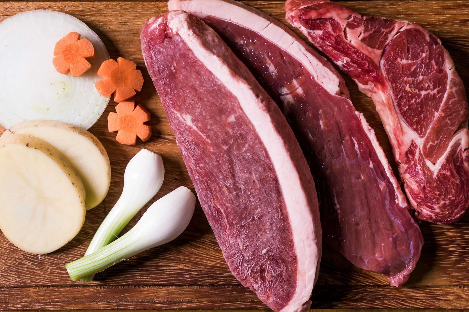 Raw steak and vegetables on a wooden surface.