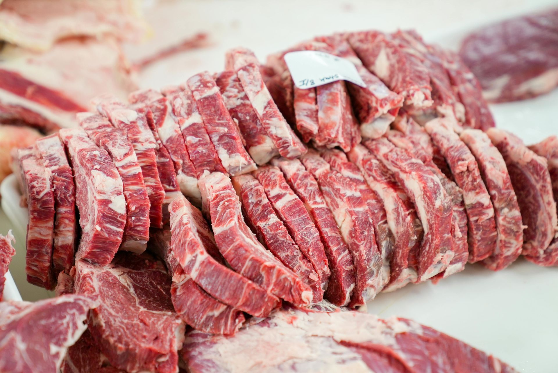 Sliced raw beef arranged on a white surface, with visible red meat and white marbling.