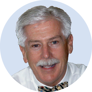 Portrait of a smiling man with gray hair and mustache, wearing a white shirt and patterned bow tie