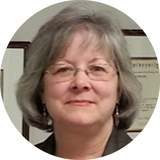 Portrait of a smiling woman with glasses and gray hair in a framed office setting