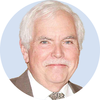 Portrait of a smiling man with white hair in a brown suit and patterned tie