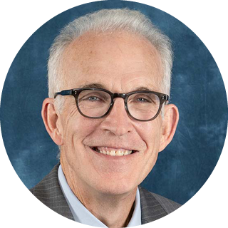 Portrait of a smiling man wearing glasses and a gray suit against a blue background