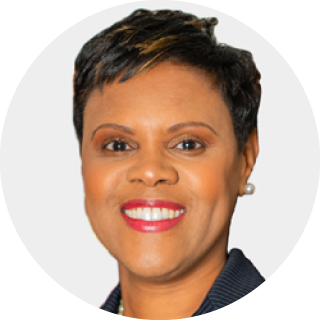 Smiling woman with short dark hair in a navy blazer on a light gray background