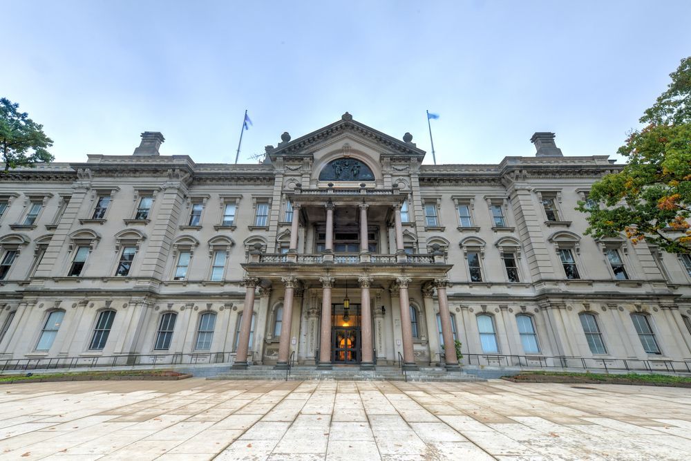 Grand neoclassical stone building with columns and a central entrance under a blue sky