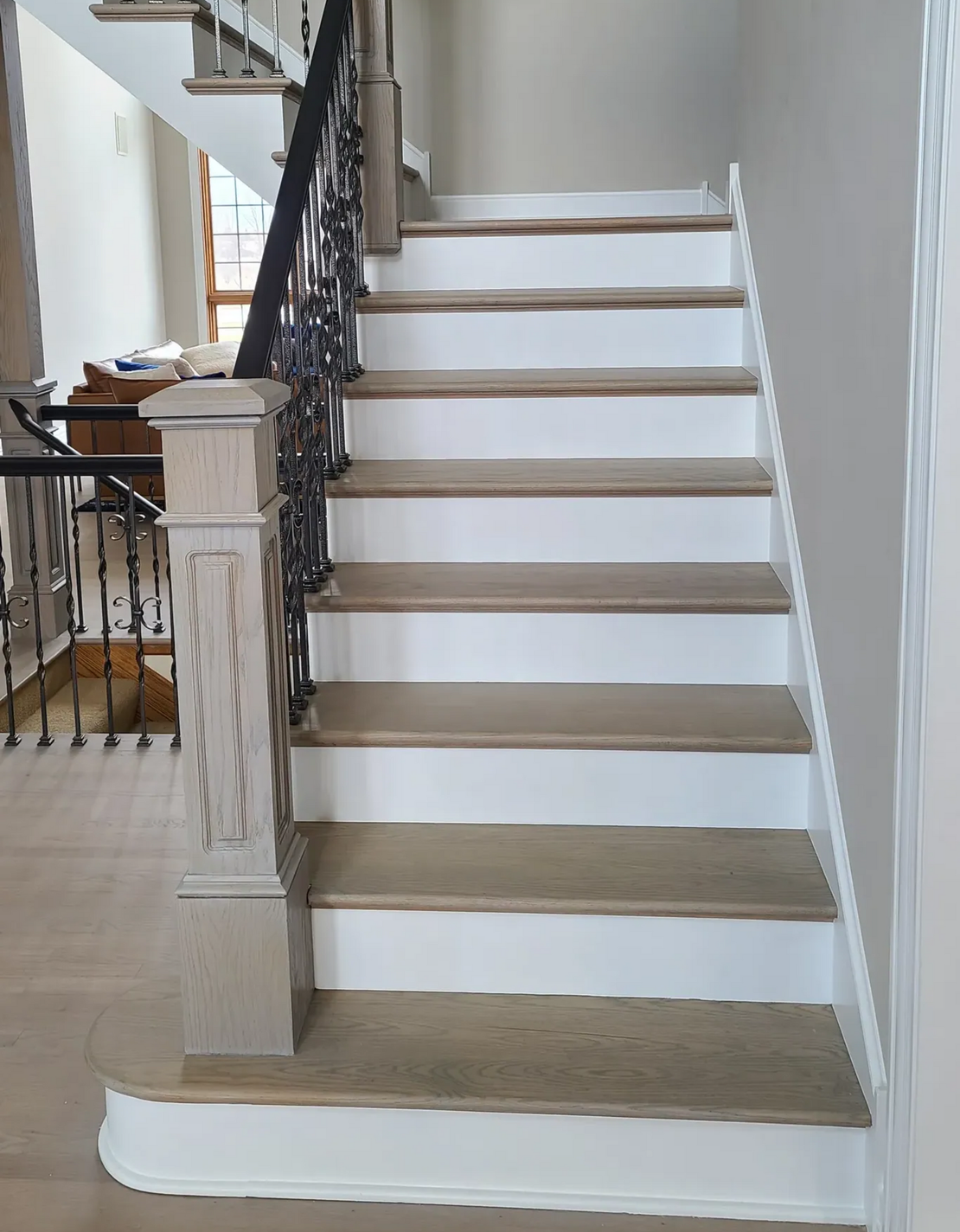 Staircase with light-colored treads, white risers, and ornate dark metal railing.