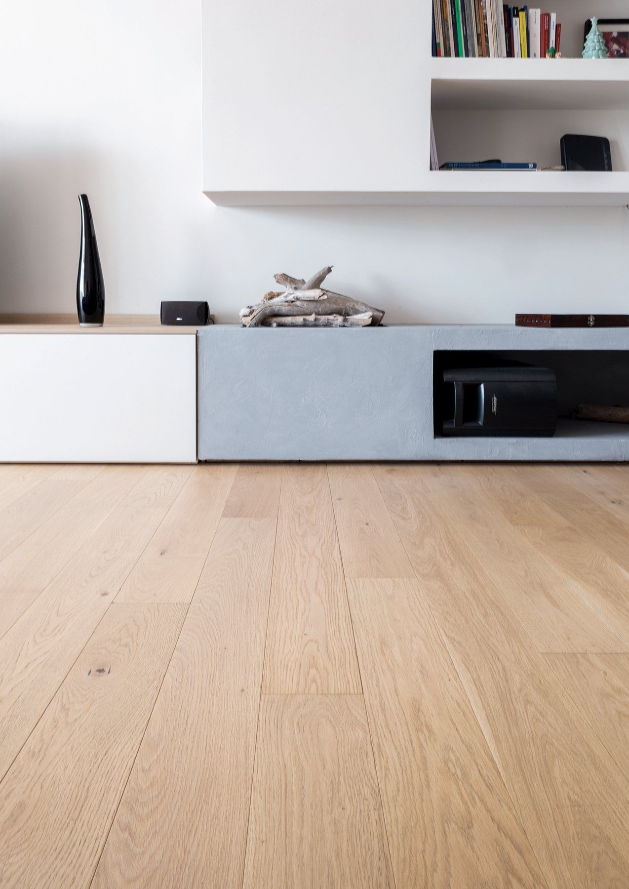 Pavimento in legno con un moderno mobiletto a muro bianco e grigio e una libreria, con decorazioni.