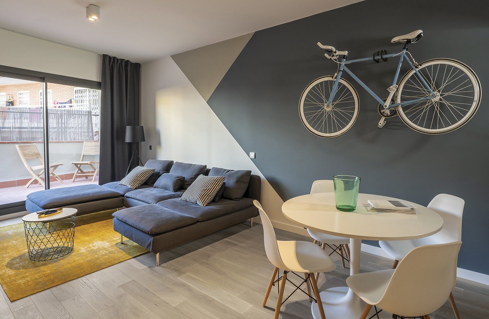 Soggiorno moderno con divano blu, bicicletta appesa al muro e piccolo tavolo da pranzo.