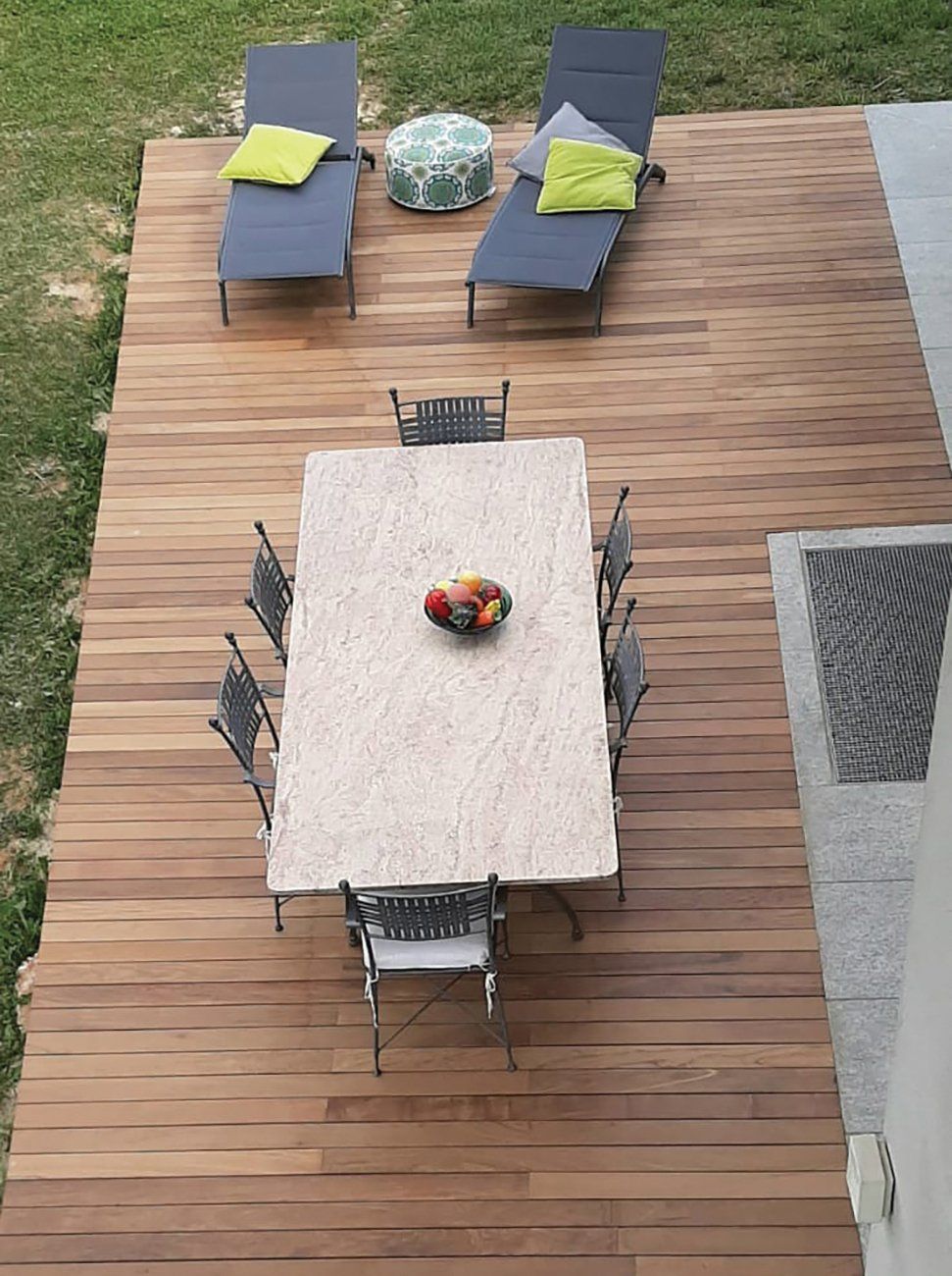 Terrazza in legno con tavolo e sedie, sedie a sdraio e un piccolo sgabello.