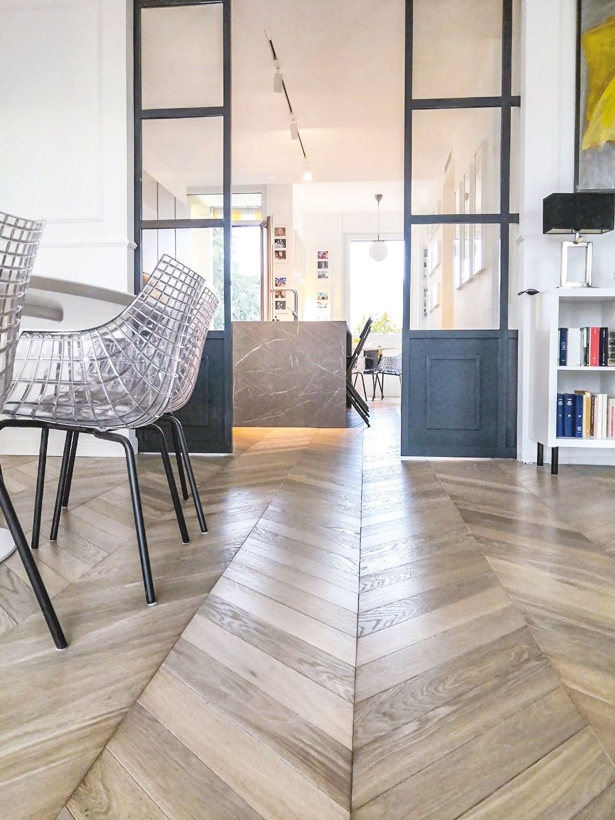 Pavimento in legno a spina di pesce che conduce alla porta con porte in vetro con telaio in metallo.