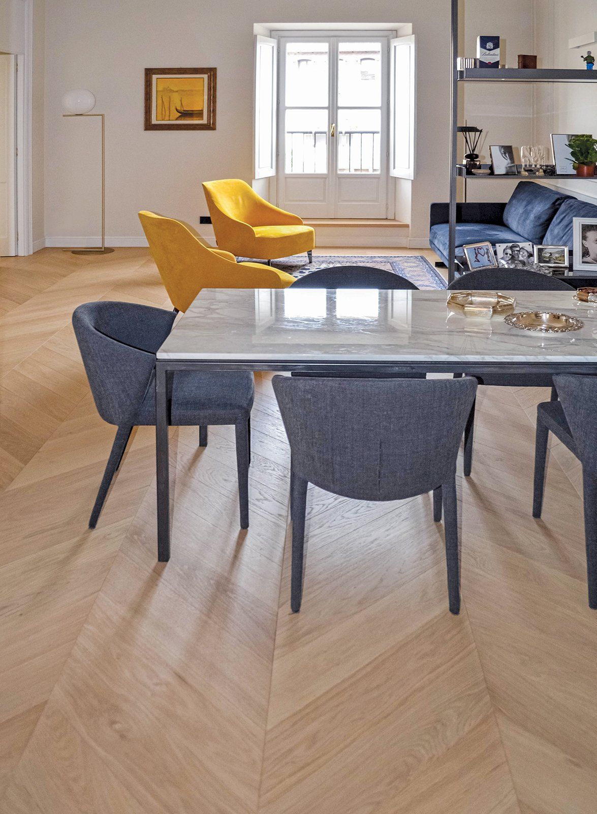 Sala da pranzo con pavimenti in legno chiaro, tavolo con piano in marmo, sedie grigie e poltrone gialle.