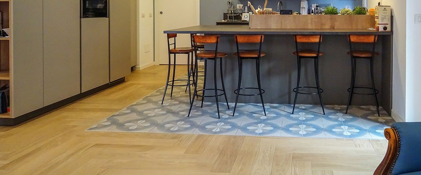 Cucina con pavimento in legno e sezione piastrellata a motivi davanti all'isola con sgabelli da bar.