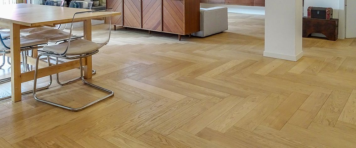 Pavimento in parquet in una stanza con tavolo, sedie e una colonna.