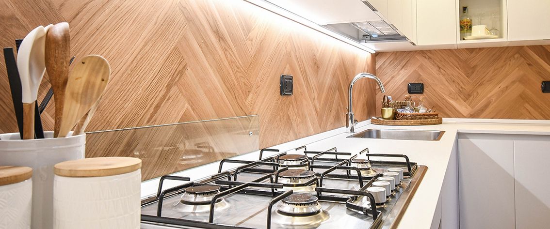 Una cucina con paraschizzi in legno a spina di pesce, fornello a gas e ripiani bianchi.