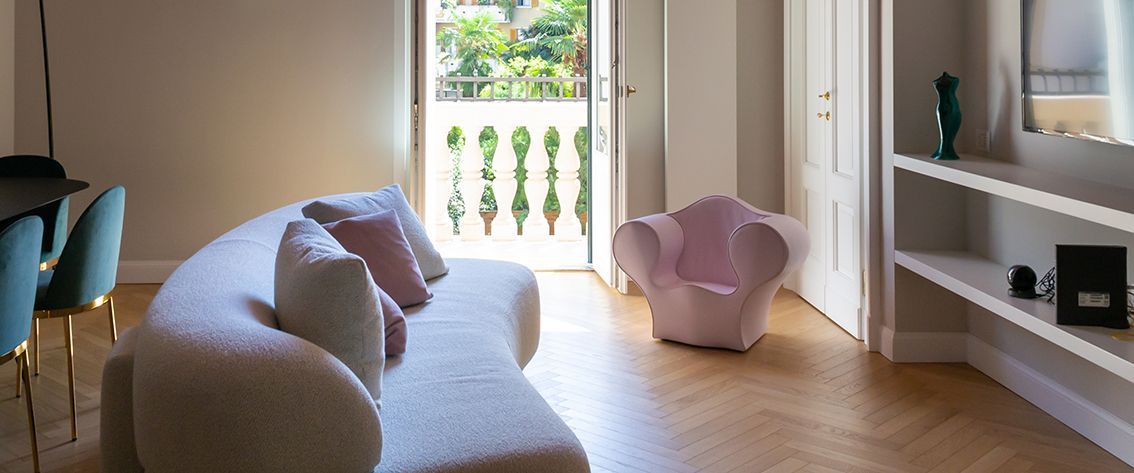 Soggiorno con divano bianco curvo, poltrona rosa e vista sul balcone.
