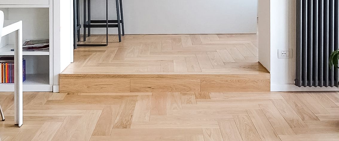 Parquet a spina di pesce con un piccolo gradino che conduce a un'altra stanza. Un termosifone si trova sulla destra.
