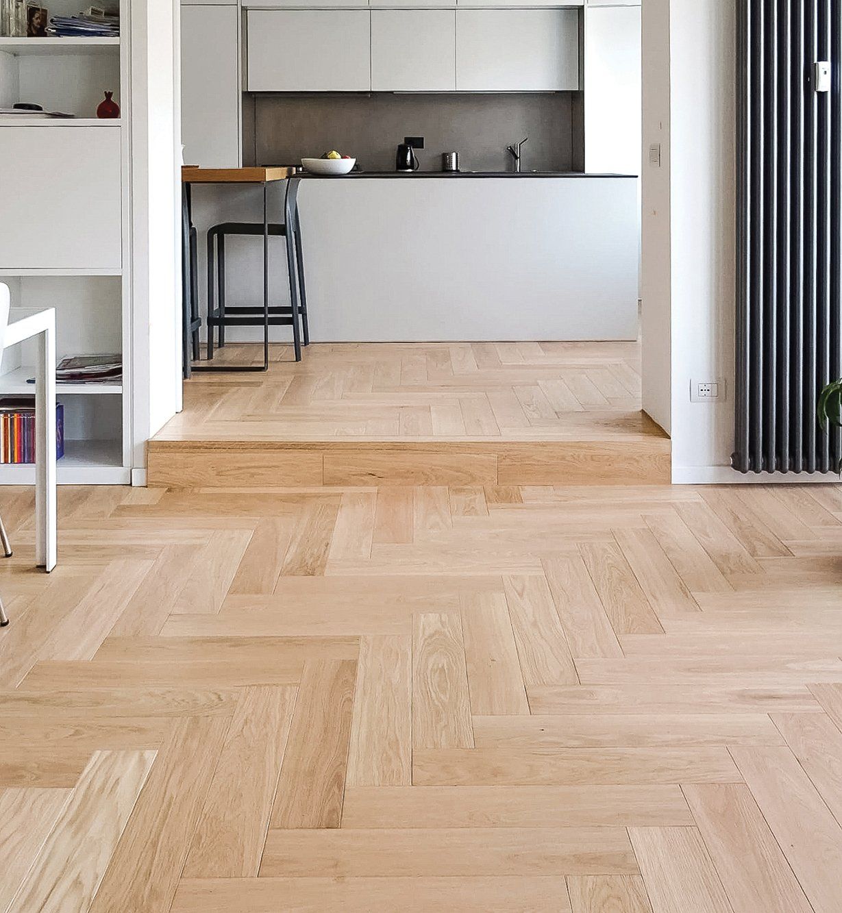 Il pavimento in legno a spina di pesce conduce a una cucina moderna con mobili bianchi e ingresso rialzato.