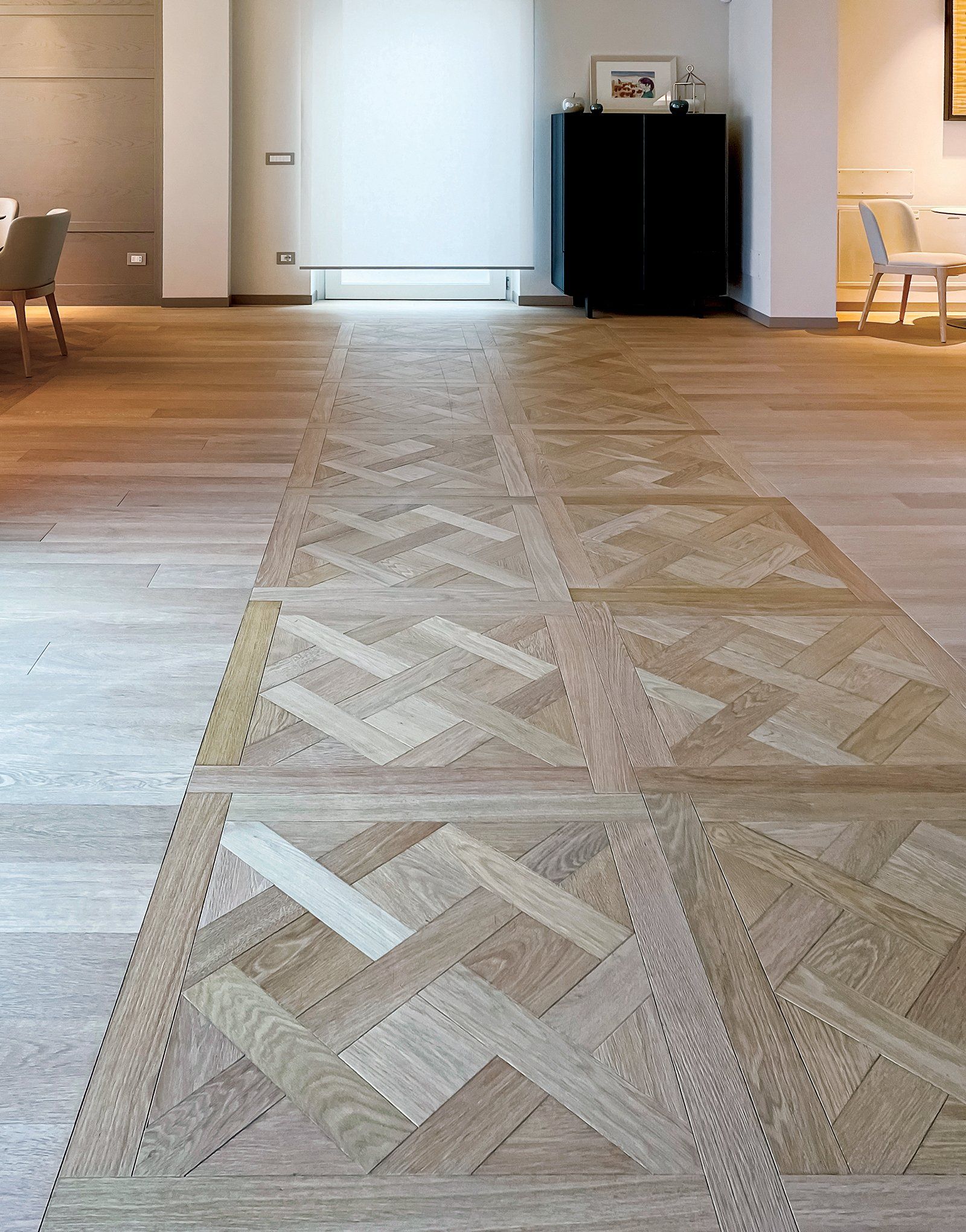 Pavimento in parquet con sezioni a motivi geometrici in una stanza dai toni chiari.