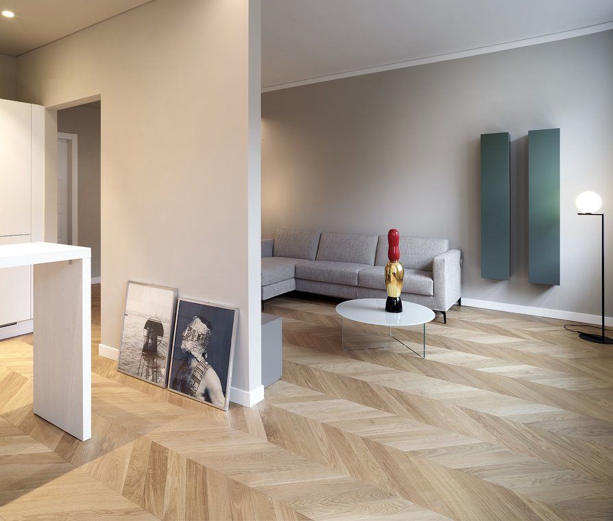 Soggiorno moderno con pavimenti in legno a spina di pesce, pareti grigio chiaro e termosifoni a parete color verde acqua.