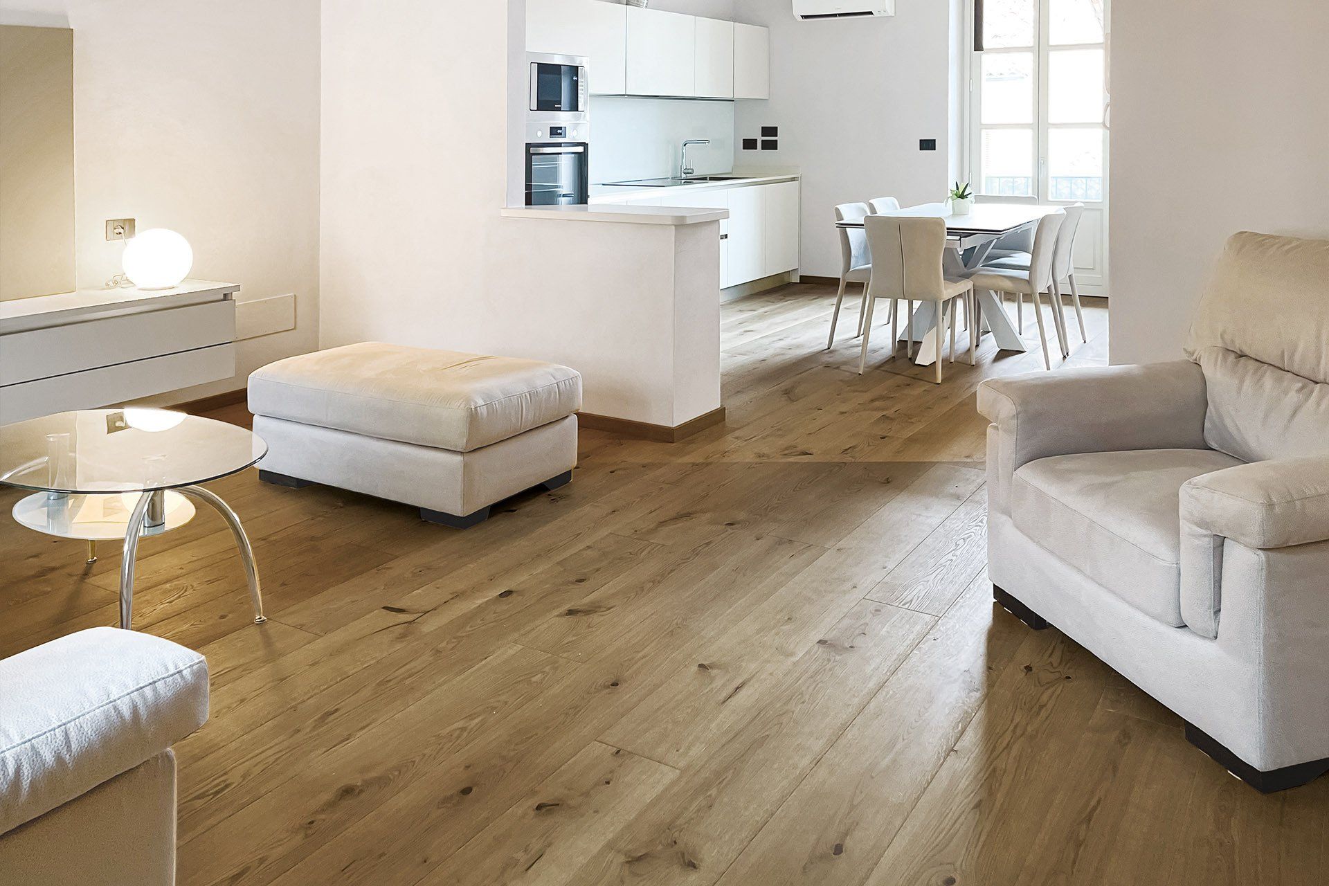Soggiorno moderno con pavimenti in legno chiaro, mobili bianchi e cucina a vista.