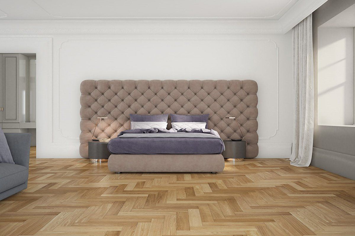Camera da letto con ampia testiera imbottita, letto con lenzuola blu, pavimenti in legno e luce naturale.