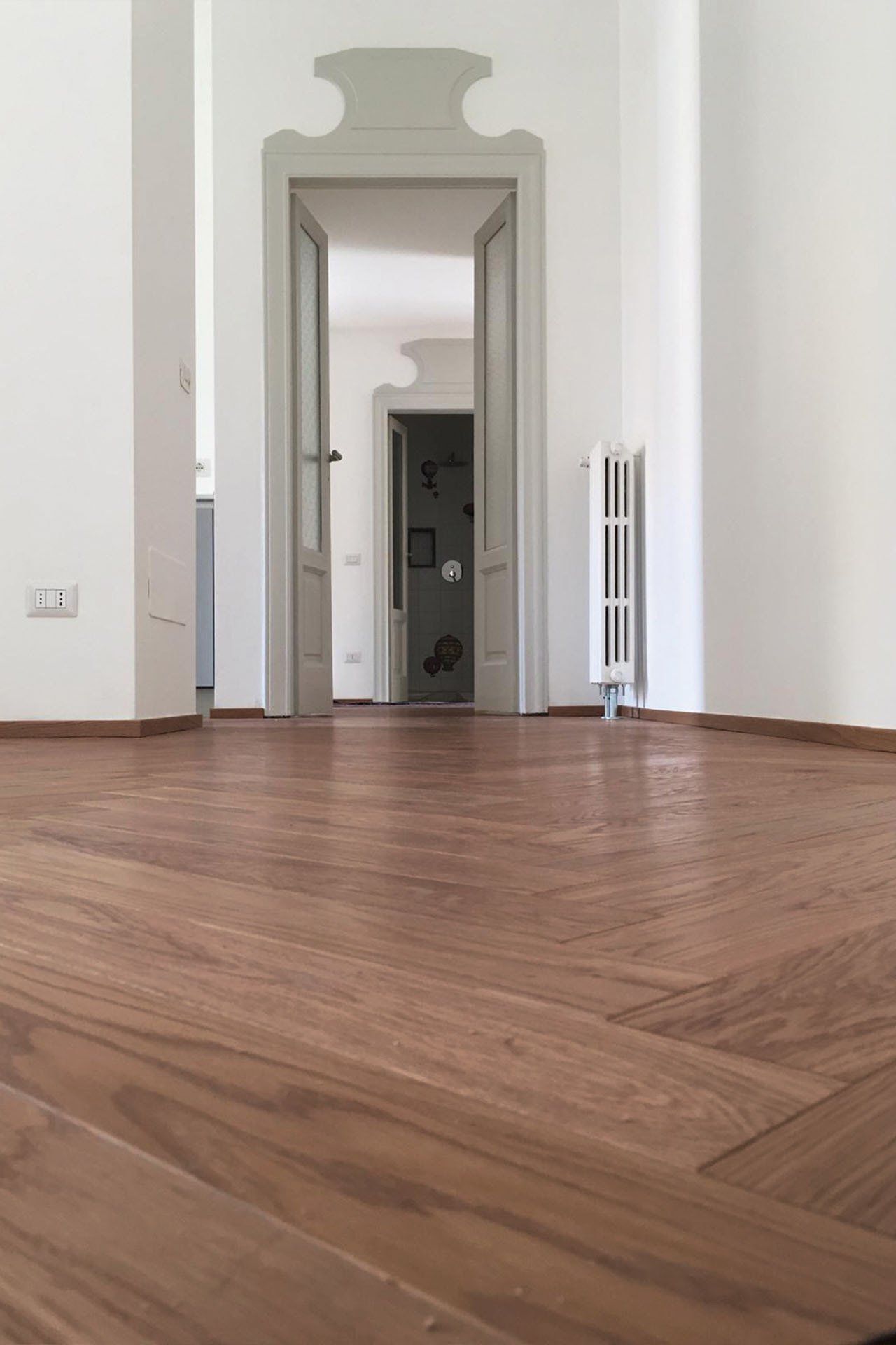 Il pavimento in legno a spina di pesce conduce a una porta aperta con pareti bianche