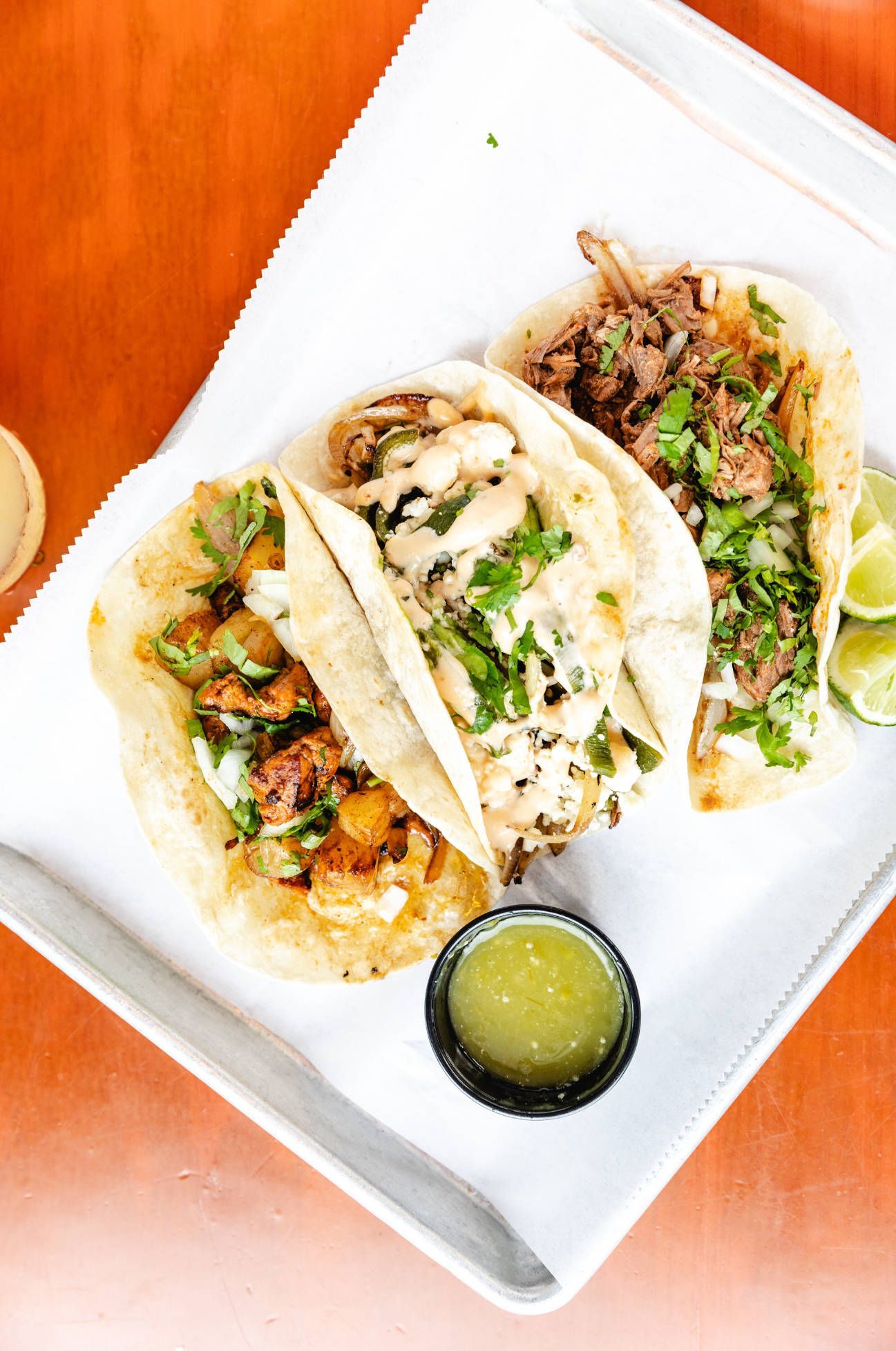 Three tacos are sitting on a white plate on a wooden table.