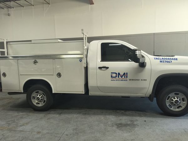 White utility truck with ladder rack and DMI logo parked indoors in a garage.