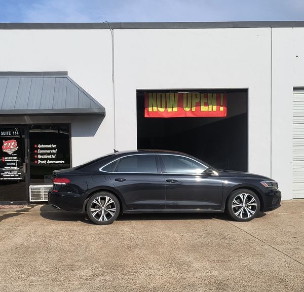 Dark sedan parked outside a white building with a neon “NOW OPEN” sign.