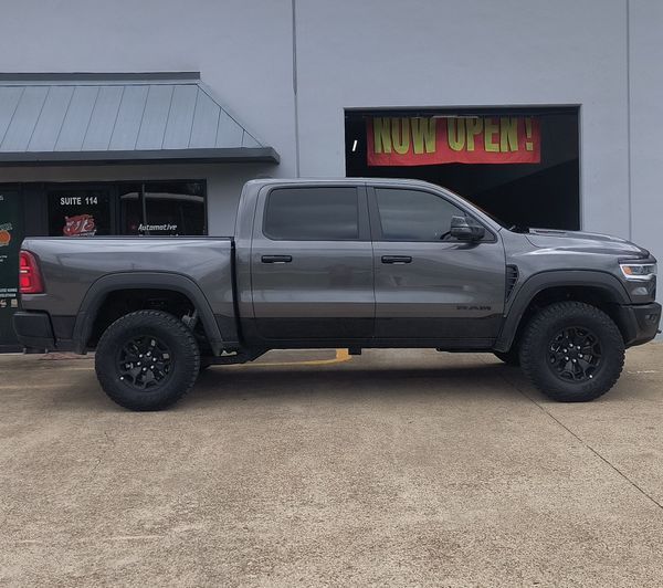 Gray lifted pickup truck parked in front of a shop with a red “NOW OPEN” sign