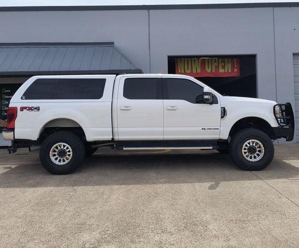 White pickup truck parked outside a building with a neon “OPEN” sign in the window