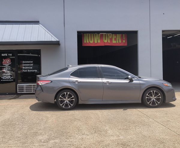 Gray sedan parked outside a building with a bright “NOW OPEN” sign above the entrance