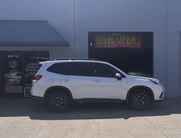 White SUV parked outside a storefront with a neon sign.