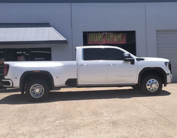 White pickup truck parked outside a building with garage doors and a sign above the entrance.