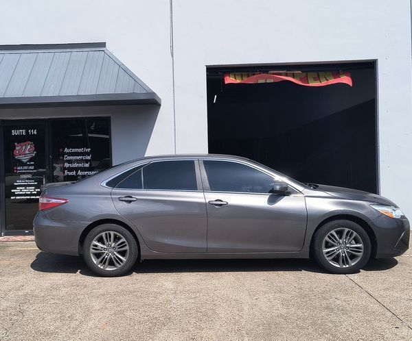 Gray sedan parked outside a shop with a black garage door and storefront window