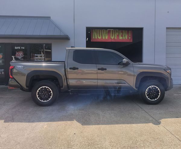 Gray pickup truck parked outside a building with a neon “NOW OPEN” sign in the window.