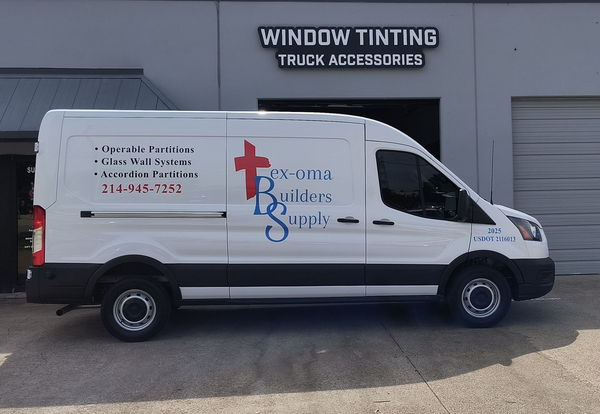 White cargo van with “Roma Builders Supply” signage parked outside a window tinting truck accessories shop.