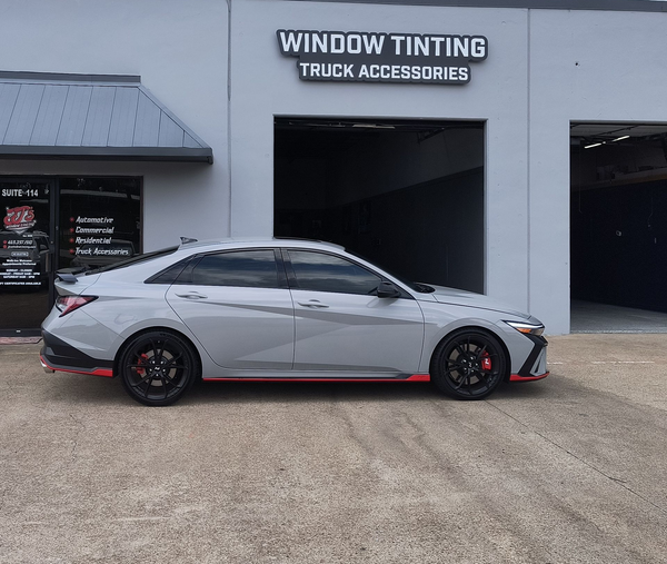 Silver sports sedan with black and red accents parked outside a window tinting and truck accessories shop