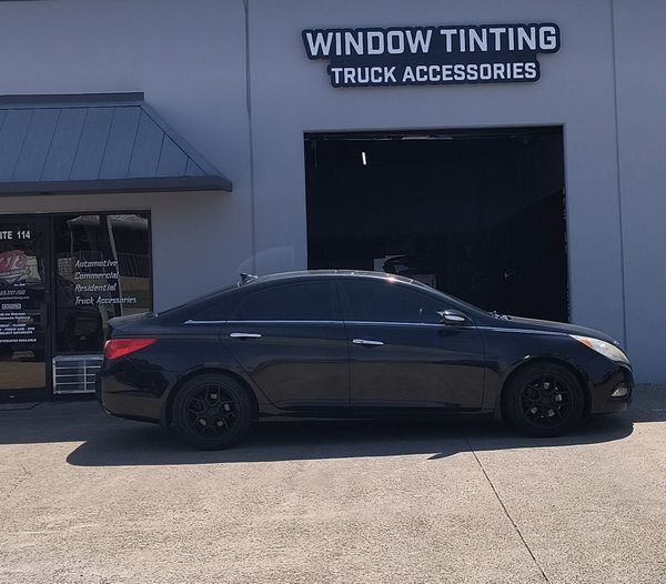 Dark gray sedan parked outside a window tinting truck accessories shop